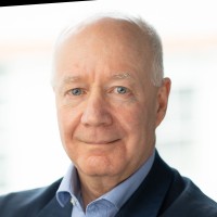 Headshot of an older man with gray hair wearing a dark jacket over a blue shirt.